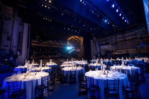 Grand venue with round tables, candlelit centerpieces, and stage lighting