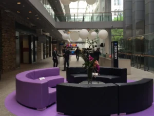 a group of people standing around a circular area with purple and black couches